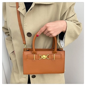 Detailed view of caramel brown handbag featuring gold heart buckle on beige trench coat