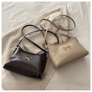 Detail of dark coffee and beige underarm bags with elegant golden bow buckles on a blazer