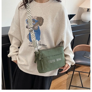Detail of green corduroy crossbody bag featuring TOTE BAG embroidery and geometric strap