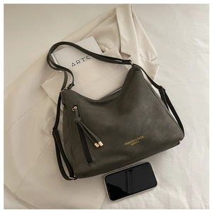 Detail of olive green suede tote bag with fringe charm and fashion logo on beige suit