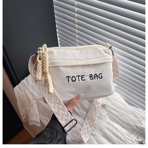 Detail of cream corduroy crossbody bag with TOTE BAG embroidery and wave pattern strap