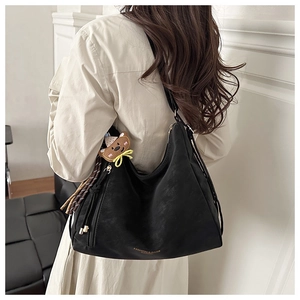 Detail of black faux leather tote bag featuring gold lettering and cute bear charm