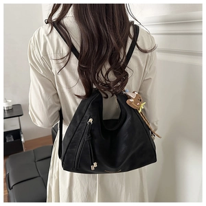 Detail view of black hobo shoulder bag with gold logo and plush bear charm accessory