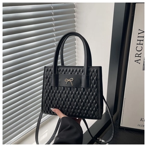 Détail d'un sac à main noir matelassé avec nœud doré et surface texturée élégante