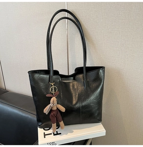 Detail of black pleated leather tote bag with a cute rabbit plush pendant and long straps