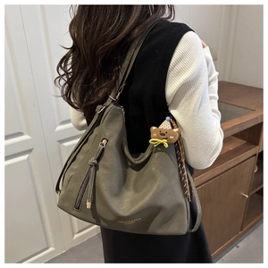 Detail of olive green suede tote bag featuring a cute bear pendant and long tassel charm
