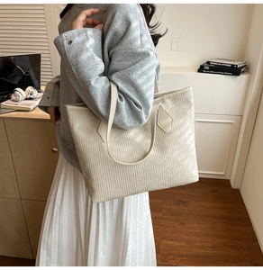 Detailed view of cream woven texture tote bag worn by a model in office setting