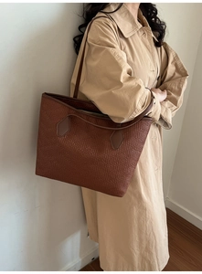 Close-up of brown textured leather tote bag carried by a model in a beige trench coat