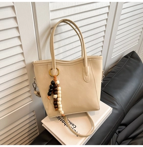 Detail of beige PU leather bucket bag with decorative beads and stylish lettering