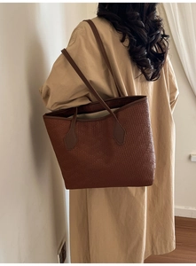 Detail showing the brown woven texture and slim leather straps on the elegant tote bag