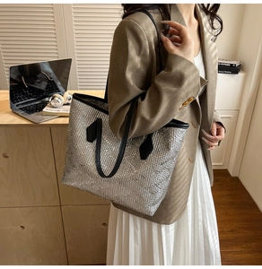 Silver woven tote bag with black handles held by model in professional office setting