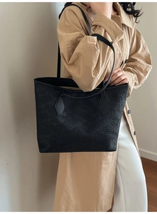 Close-up of black woven texture tote bag worn with stylish casual autumn trench coat