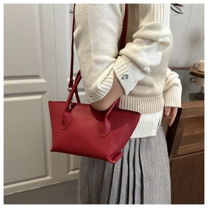 Red pebbled leather tote bag with wing silhouette worn by model in casual style