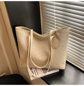 Detail of cream woven tote bag with pleated texture and smooth leather strap on windowsill