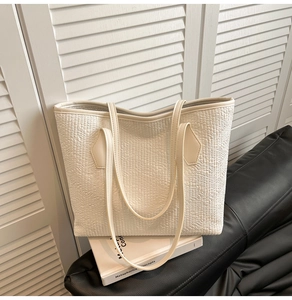 Close-up of white woven-texture tote bag on a black leather sofa with shutter background