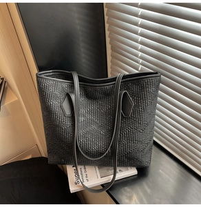 Detail shot of black tote bag featuring vertical pleated texture and sturdy double straps