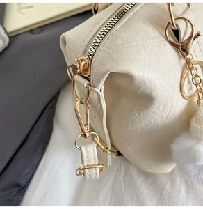 Detail einer cremeweißen Handtasche aus Kieselleder mit Goldreißverschluss und Plüschball