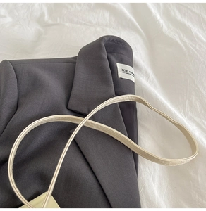 Detail von dunkelgrauem Twill-Blazer-Kragen und beige Lederriemen auf weißem Stoff
