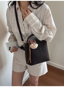 Close-up of a brown leather bucket bag featuring a decorative fringe charm on a model