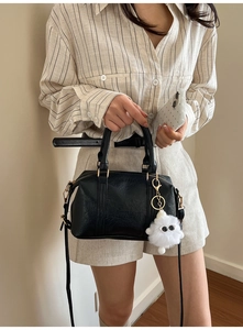 Detail of black leather handbag with embossed lettering and plush monster charm