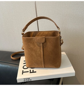 Detail of a dark brown suede bucket bag with a wide handle on a white fashion book