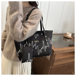 Detail of black embossed tote bag with logo plate and detachable mini pouch on shoulder