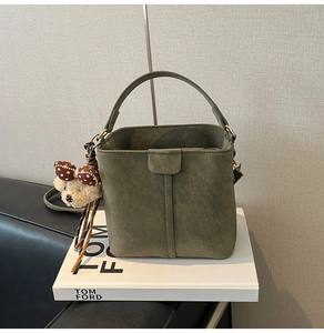 Detail of dark green suede bucket bag with a plush bear pendant and adjustable strap