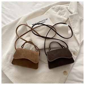 Detail of suede crossbody bags in brown and coffee on a white corduroy blazer background