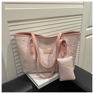 Detail of pink tote bag with wavy embroidery and golden logo plate on a white stand