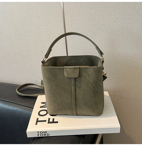 Detail of dark green matte bucket bag with adjustable strap on white decorative books
