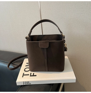 Detail of a brown bucket bag with matte suede texture and gold hardware on a book
