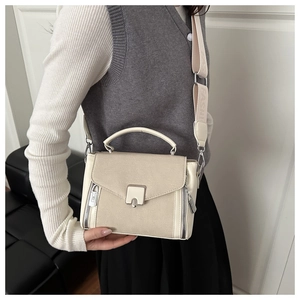 Detail of beige crossbody bag featuring side zipper accents and wide logo strap