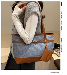 Detail of blue denim tote bag with brown leather trim and metal buckle on model