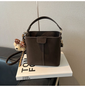 Detail of dark brown suede bucket bag with plush bear charm on Tom Ford book base