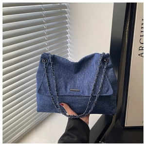Detailansicht der dunkelblauen Denim-Tasche mit Metallkette und Logo-Plakette