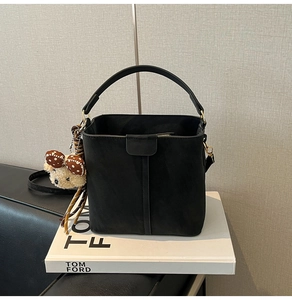 Detailed view of the black matte bucket bag with a cute bear charm and golden hardware