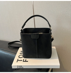 Macro detail of black suede bucket bag showing gold zipper and detachable strap