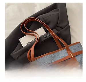 Close-up of grey felt tote bag featuring brown leather trim and golden twist lock detail