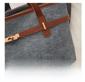 Close-up of contrast leather stitching and gold buckle on grey textured tote bag