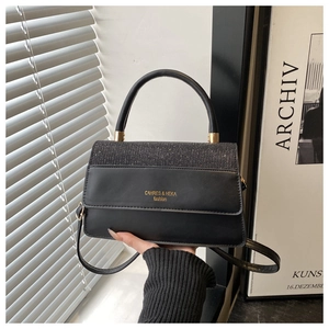 Detail of black crossbody bag with sequin patchwork and elegant top handle being held