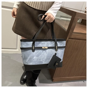 Detail of blue denim tote bag with black leather trim, gold lock and mini pouch charm