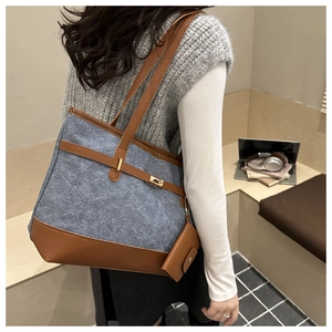 Detail of blue canvas tote bag with brown leather trim and metal belt buckle lock
