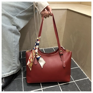 Detail of a large brick red tote bag featuring a decorative printed silk scarf on the strap