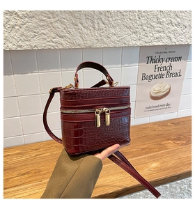 Detail of burgundy crocodile-embossed leather handbag with premium gold zipper and handle