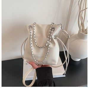 Detail of cream bucket bag showing drawstring closure and silver chain strap on art books