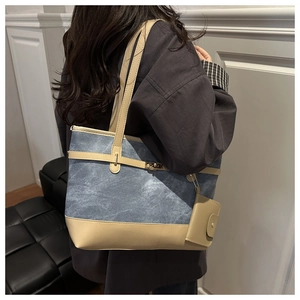 Blue denim tote bag with beige leather trim and gold buckle worn by a model