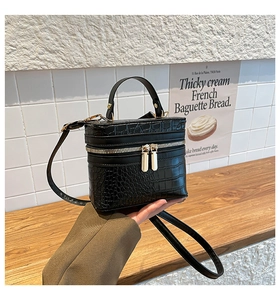 Detail of black crocodile pattern handbag with dual metal zippers and reinforced handle