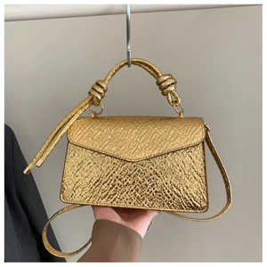 Detail view of gold textured crossbody bag featuring unique knotted top handle design