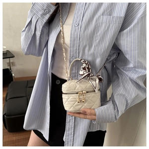 Detail of cream quilted mini bag with gold chain strap and silk scarf worn on blue shirt