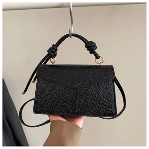 Detailed close-up of textured black small square bag with knotted handle and gold rings